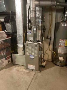 Carrier gas furnace and evaporator coil in a Buena basement, with metal exhaust venting and connected ductwork.
