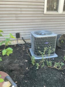 Carrier outdoor air conditioner on an equipment pad beside a Buena home, with refrigerant piping and an electrical disconnect.