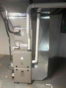 Front view of a WeatherMaker gas furnace with an evaporator coil, PVC vent pipes, and sheet-metal ductwork.