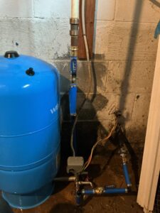 Blue well pressure tank with pressure switch and water supply piping in an Alloway Township basement.